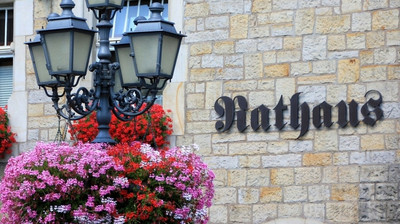 Ein Rathausgebäude. Im Vordergrund sind rosa und rot blühende Blumen.